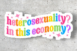 Colorful sticker with text 'heterosexuality? in this economy?' on a gray concrete background